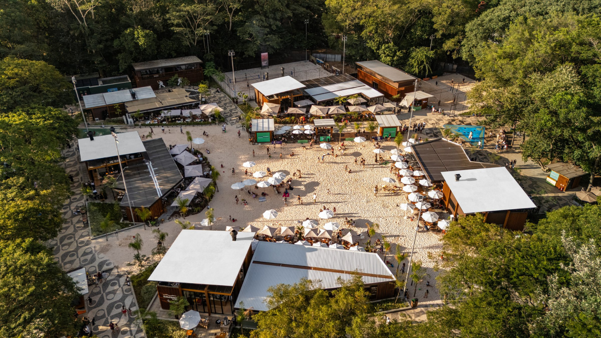 Vista aérea da Orla TotalPass no Parque Villa-Lobos, com arenas esportivas, restaurantes, área de areia e guarda-sóis